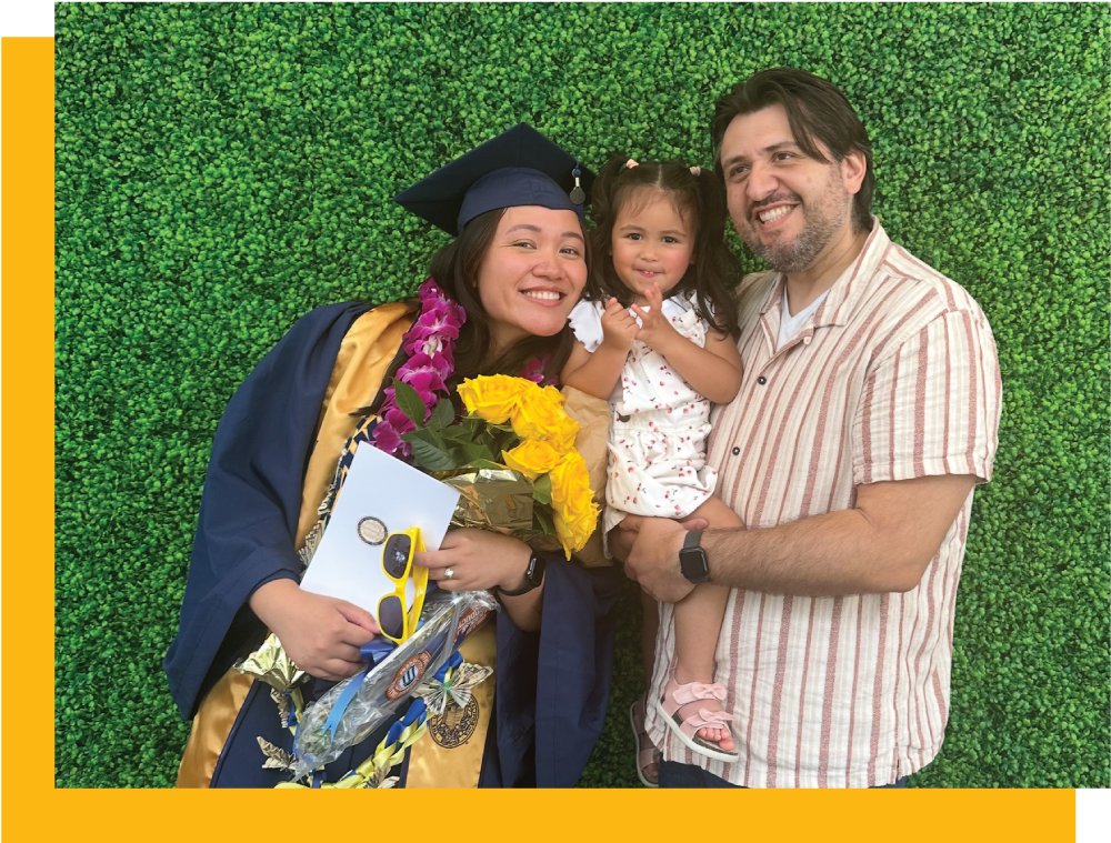 Lucky Corral in a blue graduation outfit with hat and tassle, with daughter and husband and greenery background
