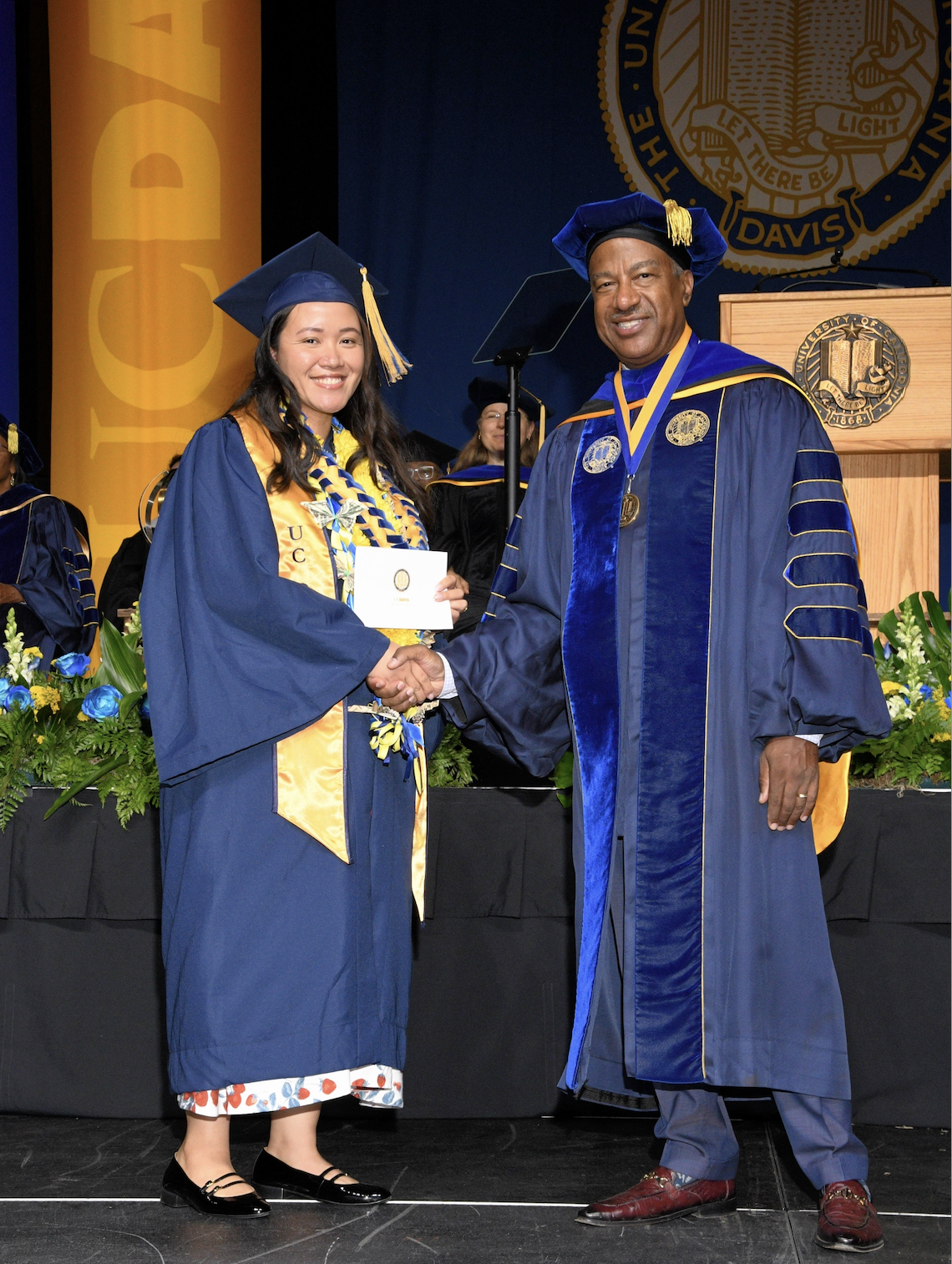 Lucky Corral in a blue graduation outfit with hat and tassle, shaking hands with dignitary who gave her her diploma