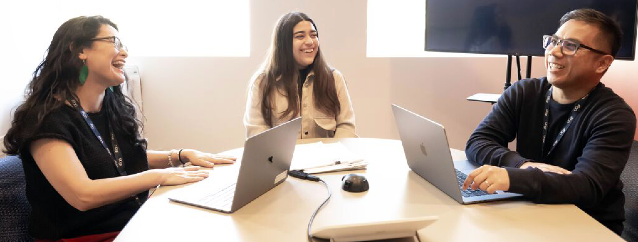 Three employees around a table with their laptops open